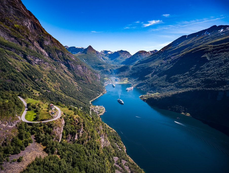 Dramatic Norwegian fjord with towering cliffs, lush green slopes and a cruise ship